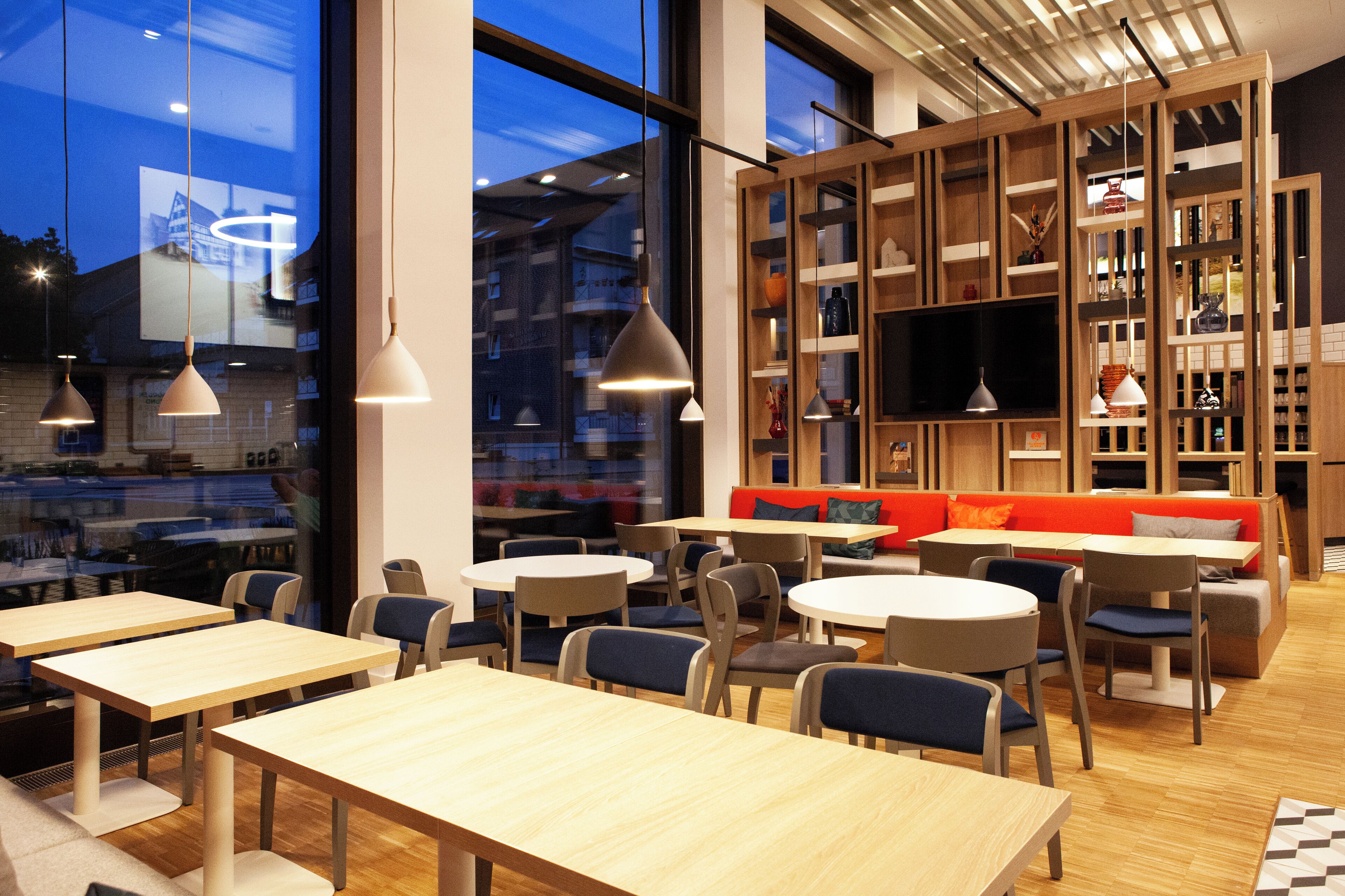 Un café moderne avec des tables et des chaises rondes, une bibliothèque en bois et un écran de télévision.