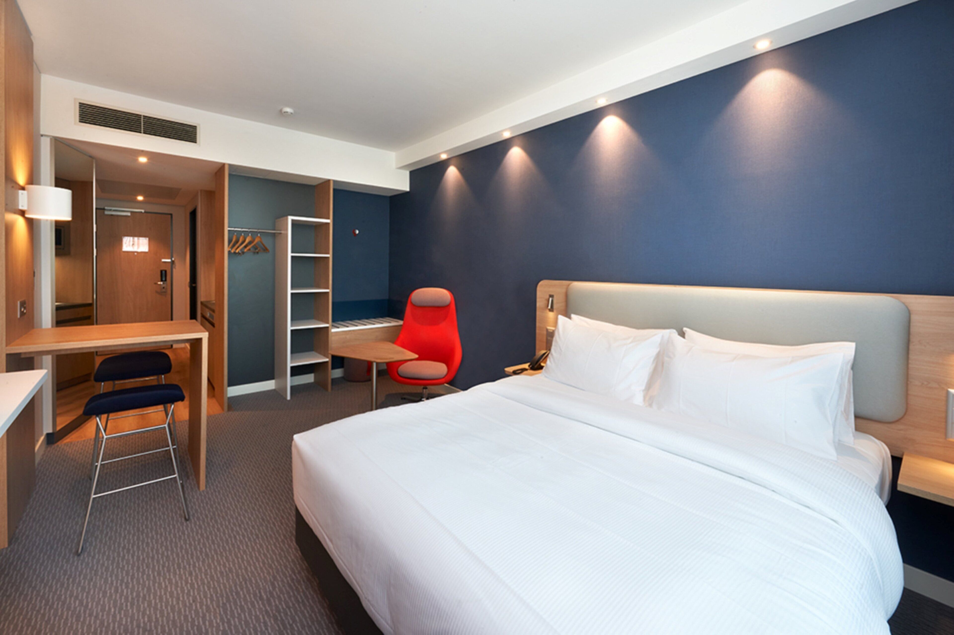 A hotel room with a bed, desk, chair, and wardrobe.