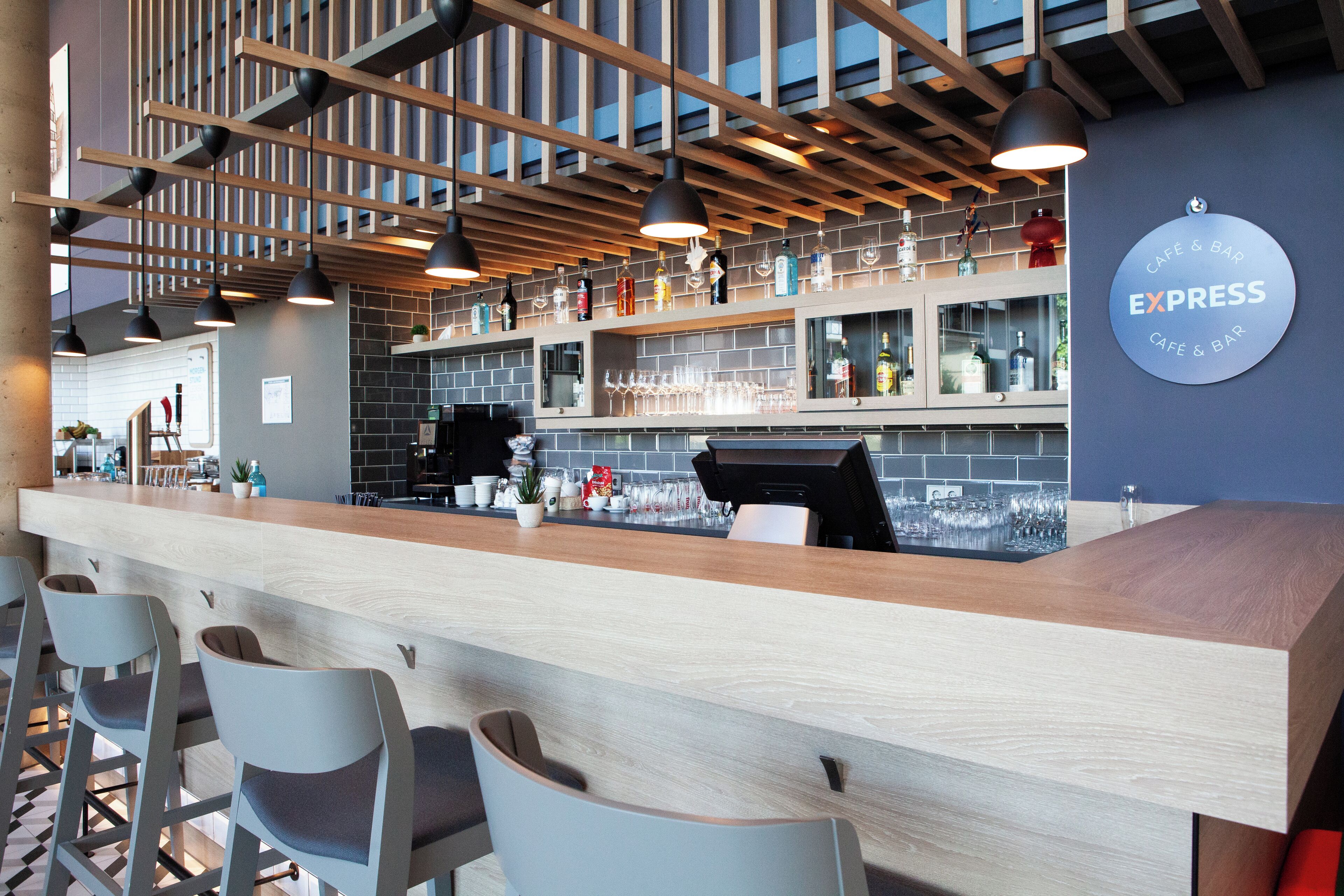 A modern bar area with a wooden counter, bar stools, and a sign reading "EXPRESS CAFE & BAR".