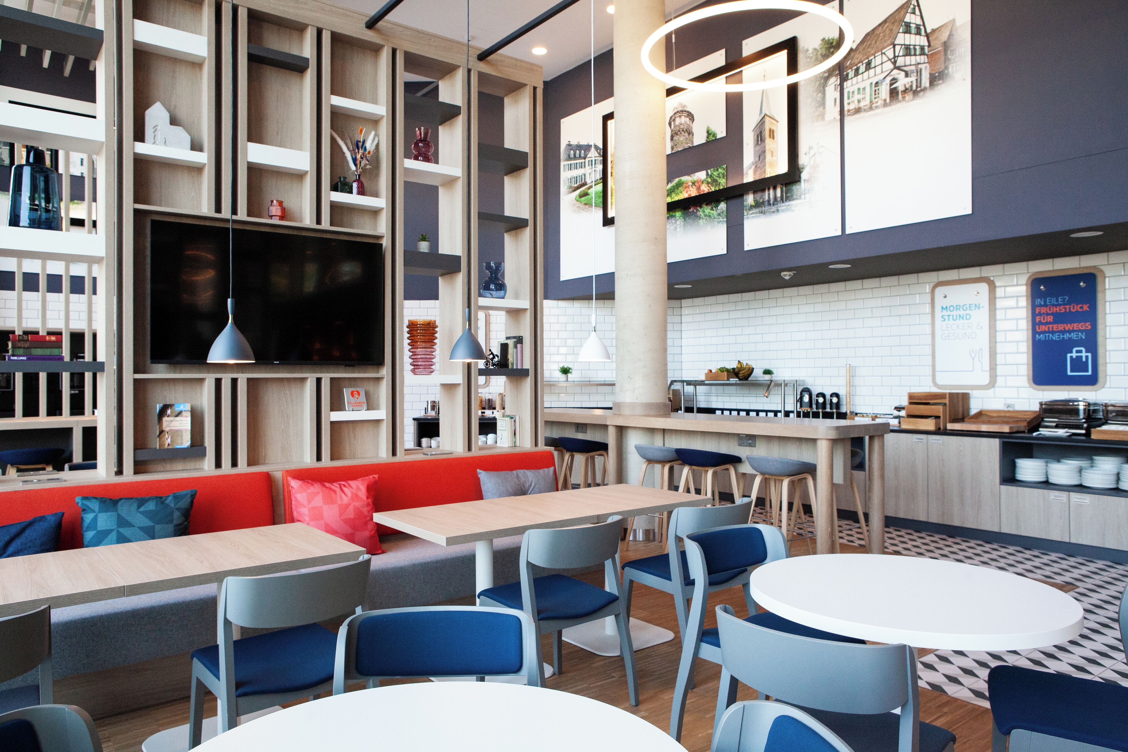 A modern restaurant with a long communal table, individual seating, and a kitchen area.