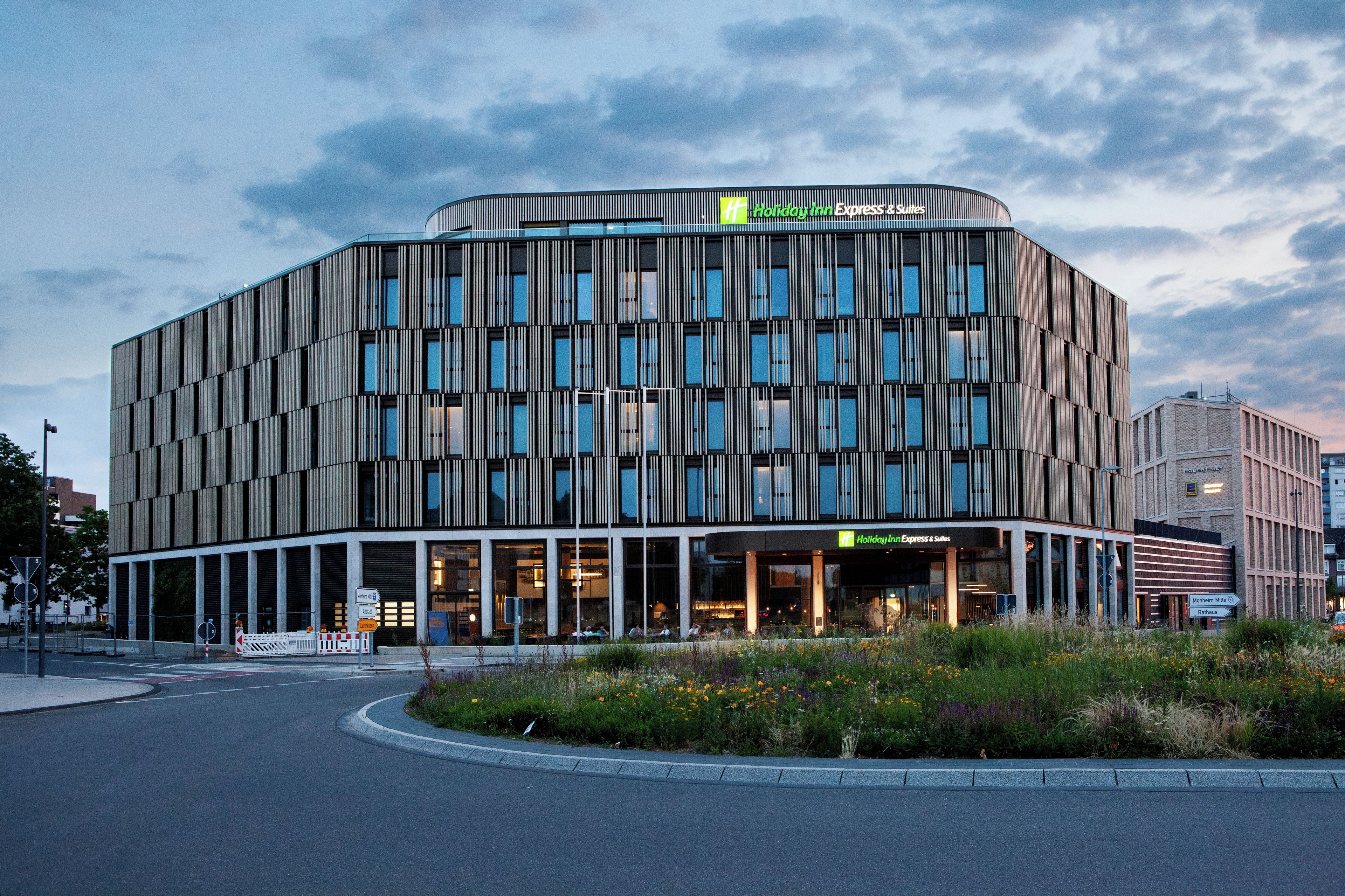 Et moderne hotel med en buet facade, mange vinduer og en anlagt have foran.