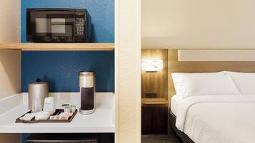 A hotel room with a microwave on a shelf, a coffee maker, and a trash bin.