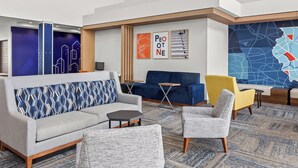 Un hall d’entrée moderne avec un canapé gris, un fauteuil bleu, un fauteuil jaune et un fauteuil à motifs. On aperçoit des casiers au fond et une grande œuvre d’art abstraite accrochée au mur.