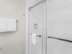 A modern bathroom with a glass shower door, a towel rack with two white towels, and a small shelf with toiletries.