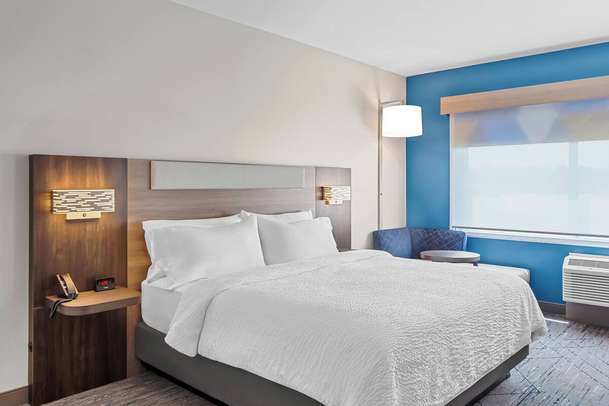 Ein modernes Hotelzimmer mit einem großen Bett, einem Nachttisch mit Telefon, einer Wandleuchte und einem Fenster mit Ausblick.