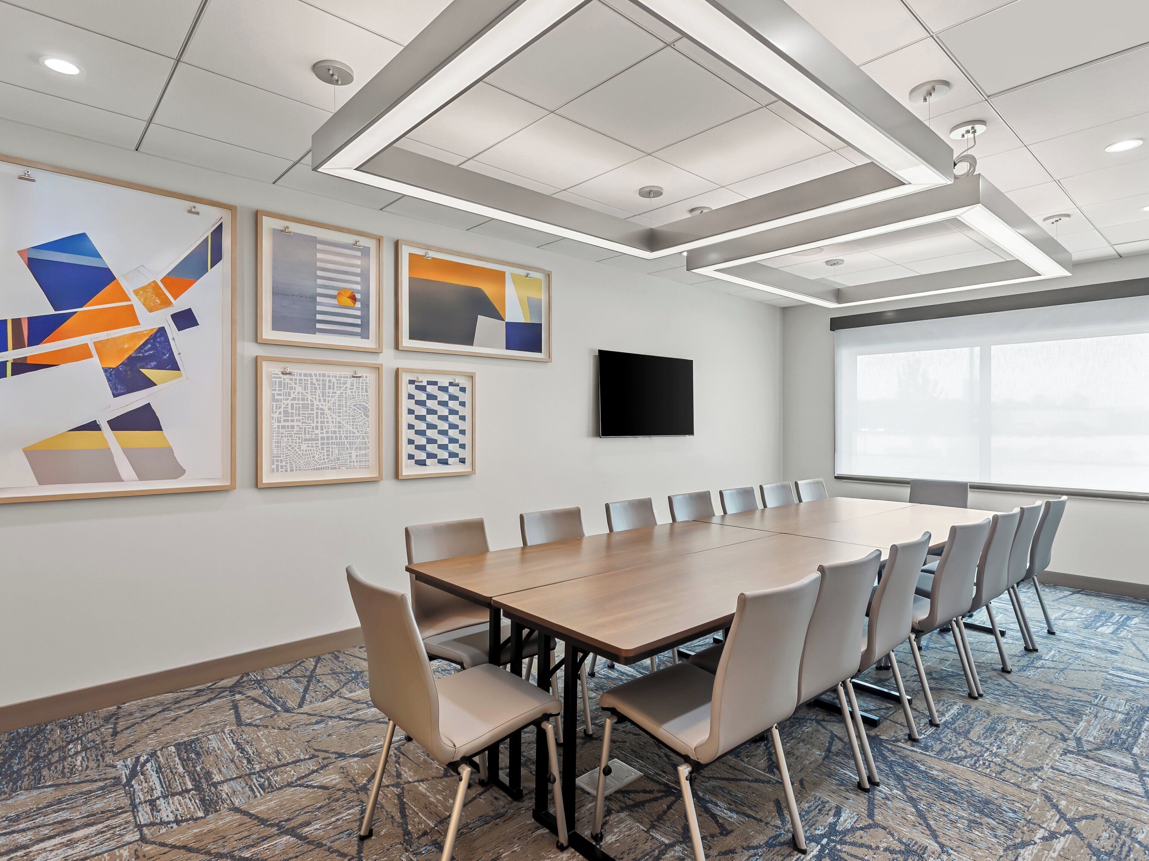 A conference room with a long table, chairs, a flat-screen TV, and framed artwork on the walls.