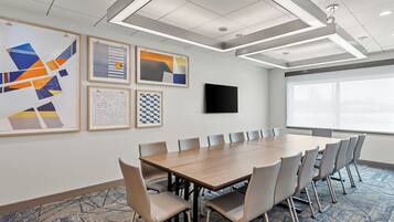 A conference room with a long table, chairs, a flat-screen TV, and framed artwork on the walls.