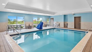 Une piscine avec une terrasse carrelée, un espace salon couvert et une vue sur l’extérieur grâce à de grandes fenêtres.