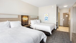 Habitación de hotel con dos camas, cabecero de madera, mesita de noche, lámpara de pared y una puerta que da a otra habitación.