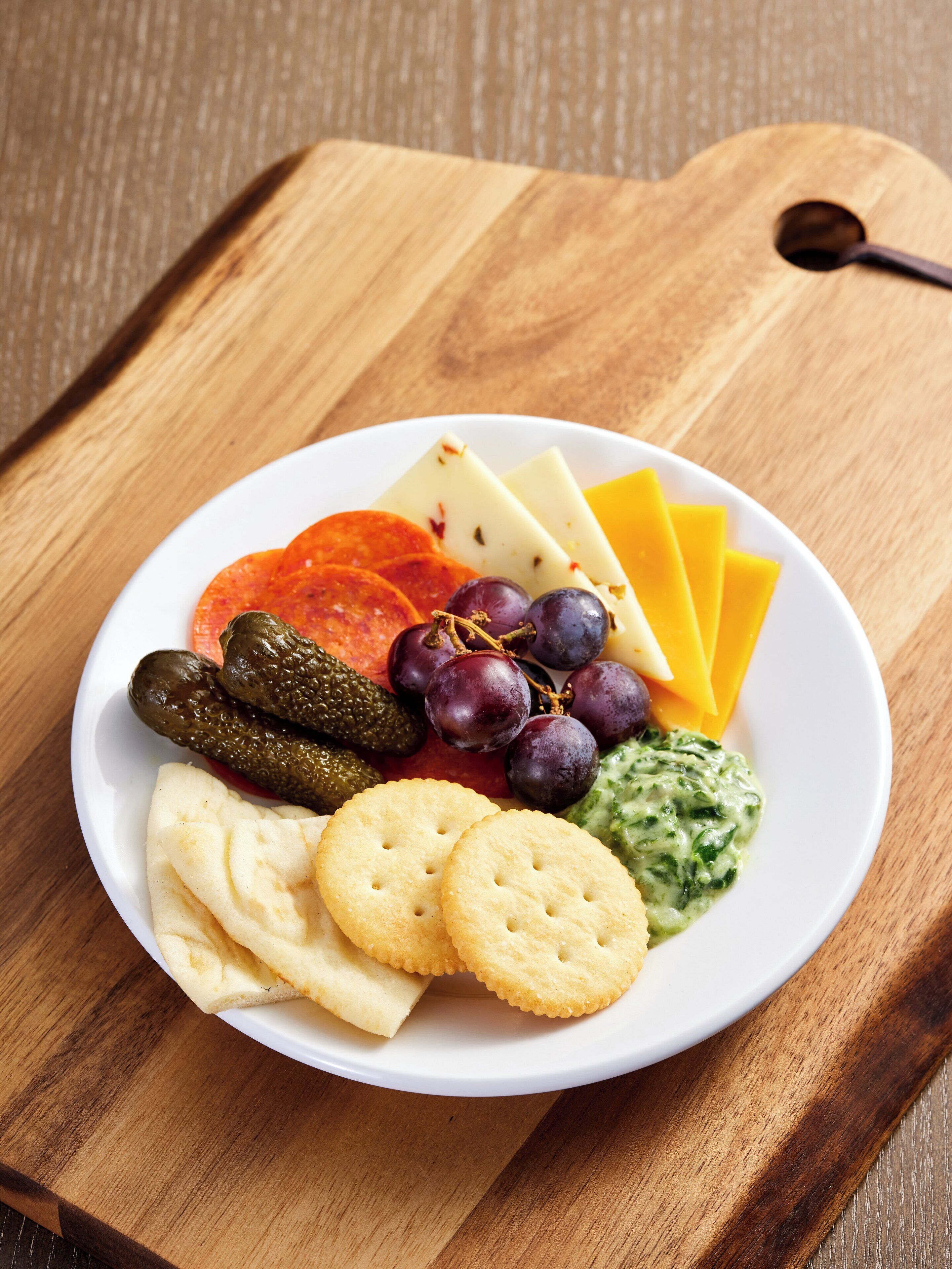 Una tabla de madera con una variedad de quesos, pepinillos, uvas y galletas.