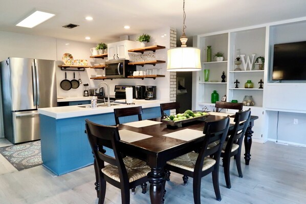 A modern kitchen with a central island, stainless steel appliances, and a dining area with wooden chairs. - PRIVATE and serene riverfront retreat - LARGE spacious yard with a cozy home! (Canyon Lake)