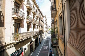 A narrow street with buildings on both sides, featuring balconies and a clear road with a speed limit sign.