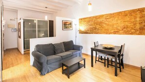 Una sala moderna con un sofá gris, una mesa de comedor de madera con sillas, una pequeña mesa de centro negra y una pared de ladrillo.