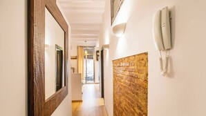 Un pasillo con piso de madera, pared de ladrillo decorativa y un teléfono en la pared, con una puerta al final.
