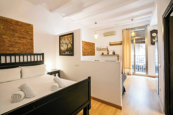 A bedroom with a bed, a wooden headboard, a painting, a shelf with decorative items, and a view of the outside balcony.