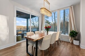 Enjoy meals in this dining area with a wooden table and six chairs, offering a view of the outdoors and a deck with a fire pit.
