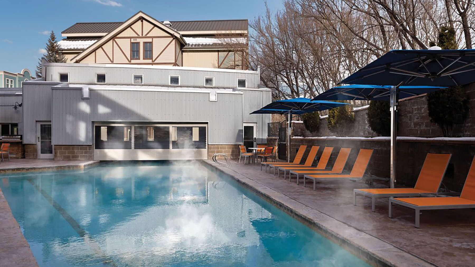 Una piscina con lettini e ombrelloni, circondata da un edificio dal design moderno.