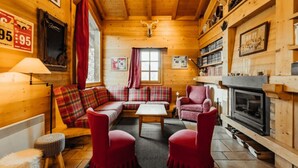 A cozy log cabin interior with a wooden ceiling, a fireplace, a sofa set, and a dining table. - Cottage with balconies in Demi-Quartier (Demi-Quartier)