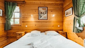 A wooden cabin room with a bed, two nightstands, a poster on the wall, and plaid curtains. - Cottage with balconies in Demi-Quartier (Demi-Quartier)