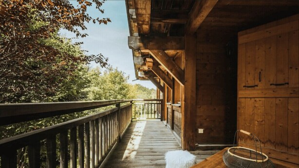 A wooden deck with a railing, a white fluffy dog, and a basket on a table. - Cottage with balconies in Demi-Quartier (Demi-Quartier)