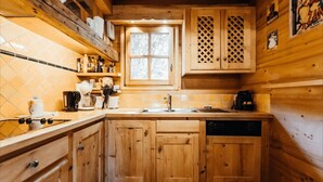 A wooden cabin-style kitchen with a window, wooden cabinets, a sink, and a dishwasher. - Cottage with balconies in Demi-Quartier (Demi-Quartier)