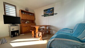 A room with a bed, a wooden table, a television, and a kitchen area. - Charming T2 in residence with swimming pool (Fleury)