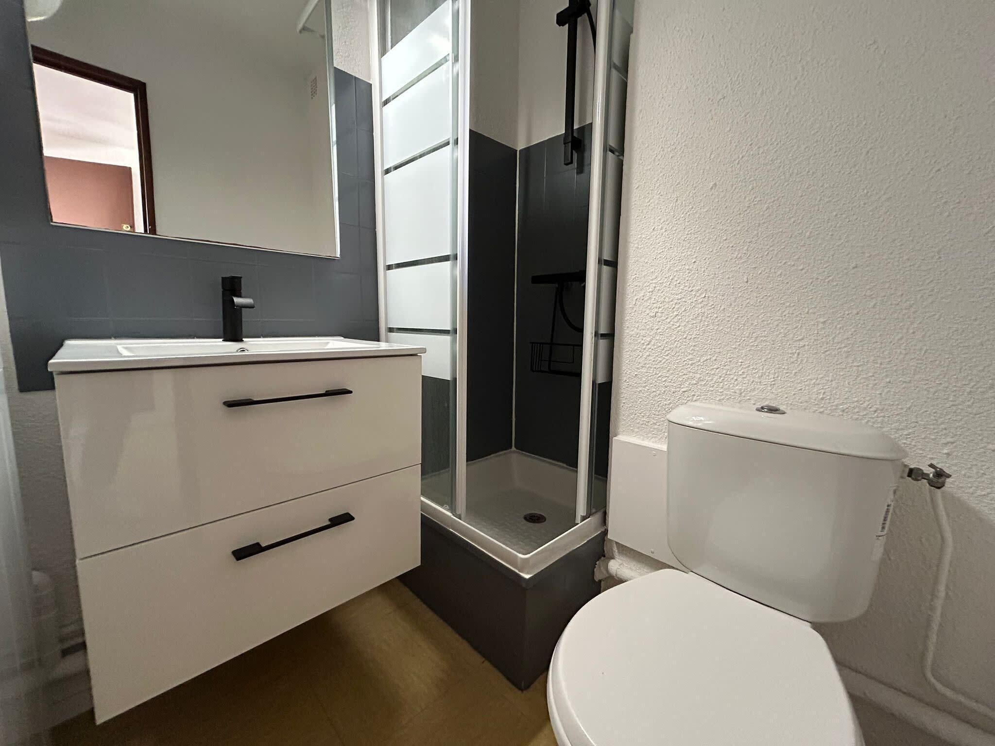 Un baño pequeño con un lavamanos blanco, un inodoro y una cabina de ducha de vidrio.