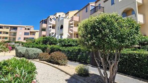 A multi-story residential building with balconies, surrounded by well-maintained gardens and hedges. - Charming T2 in residence with swimming pool (Fleury)
