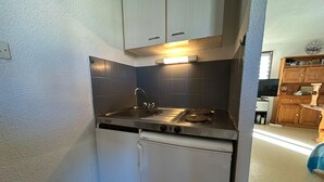 A compact kitchen with a built-in dishwasher, a stainless steel sink, and a stove. - Charming T2 in residence with swimming pool (Fleury)