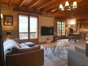 A spacious living area with a large sofa, a television, and a dining table with chairs.
