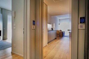 A modern hotel room with a wooden floor, a kitchenette, a dining area, and a bathroom with a shower.