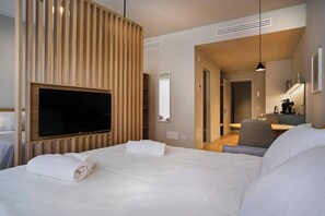 A hotel room with a large bed, a flat-screen TV mounted on the wall, a desk with a chair, and a bathroom visible through an open door.