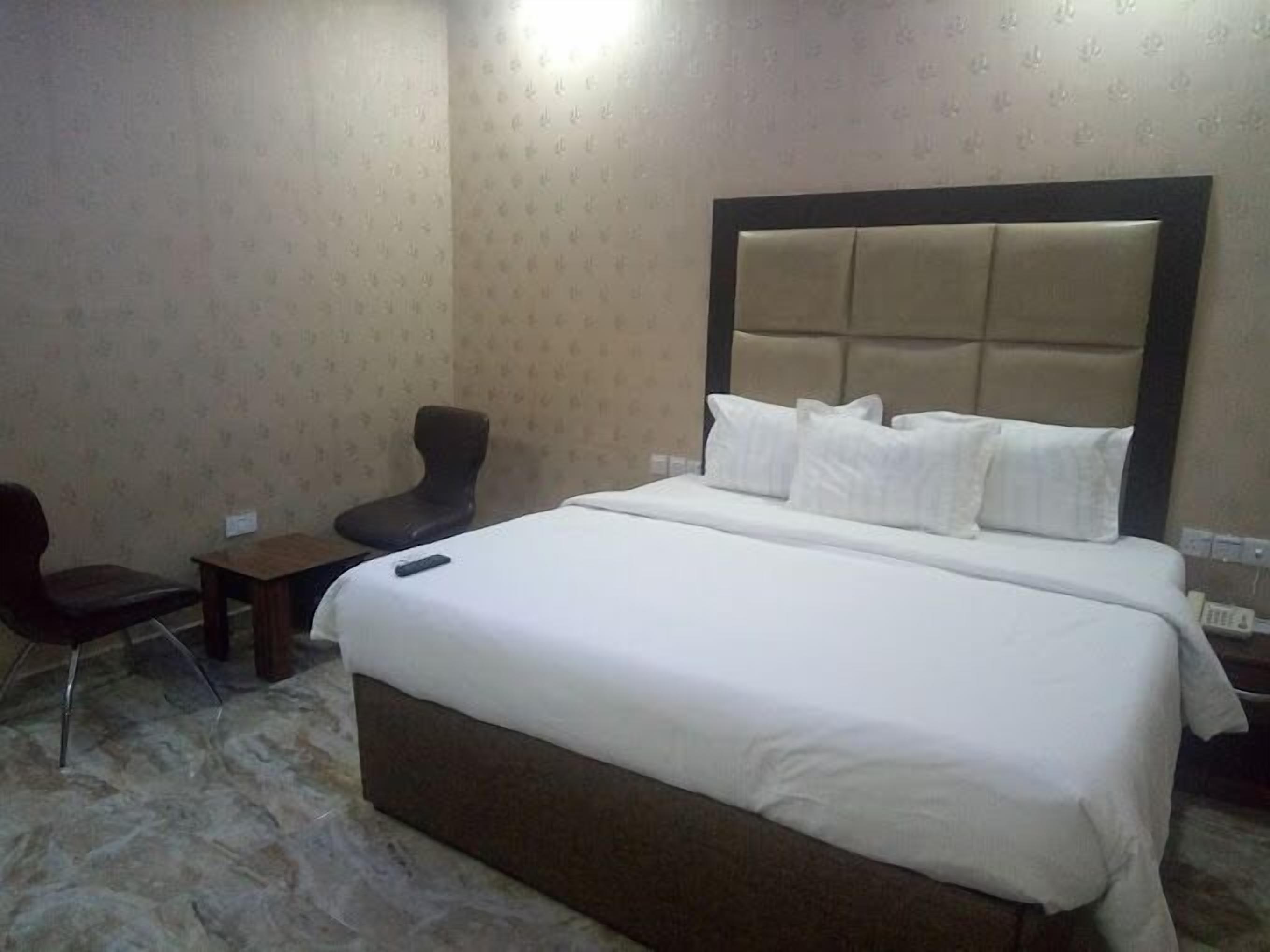 A hotel room with a large bed, a chair, a small table, and a nightstand.