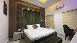A modern bedroom with a large bed, a bedside table, a green bench, and a chair. - Hiltons Bellaire (Abuja)