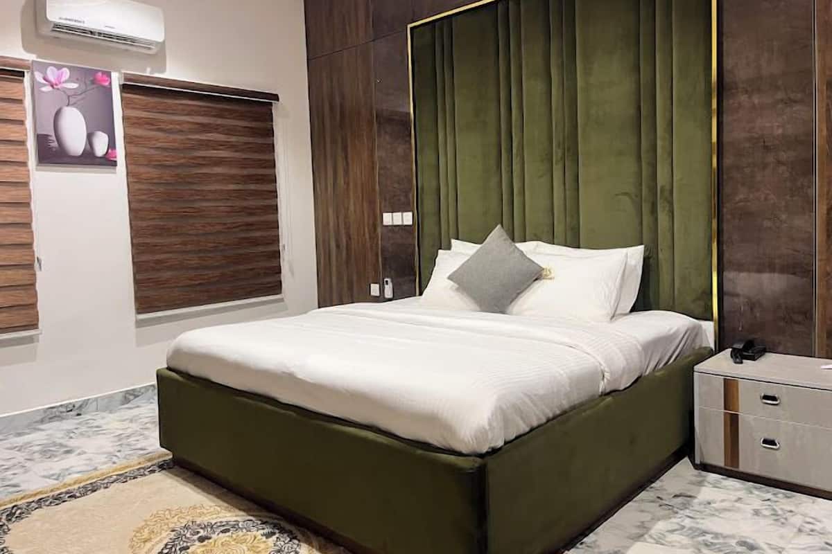 A modern bedroom with a green upholstered headboard, a white bedspread, and a marble-patterned rug.