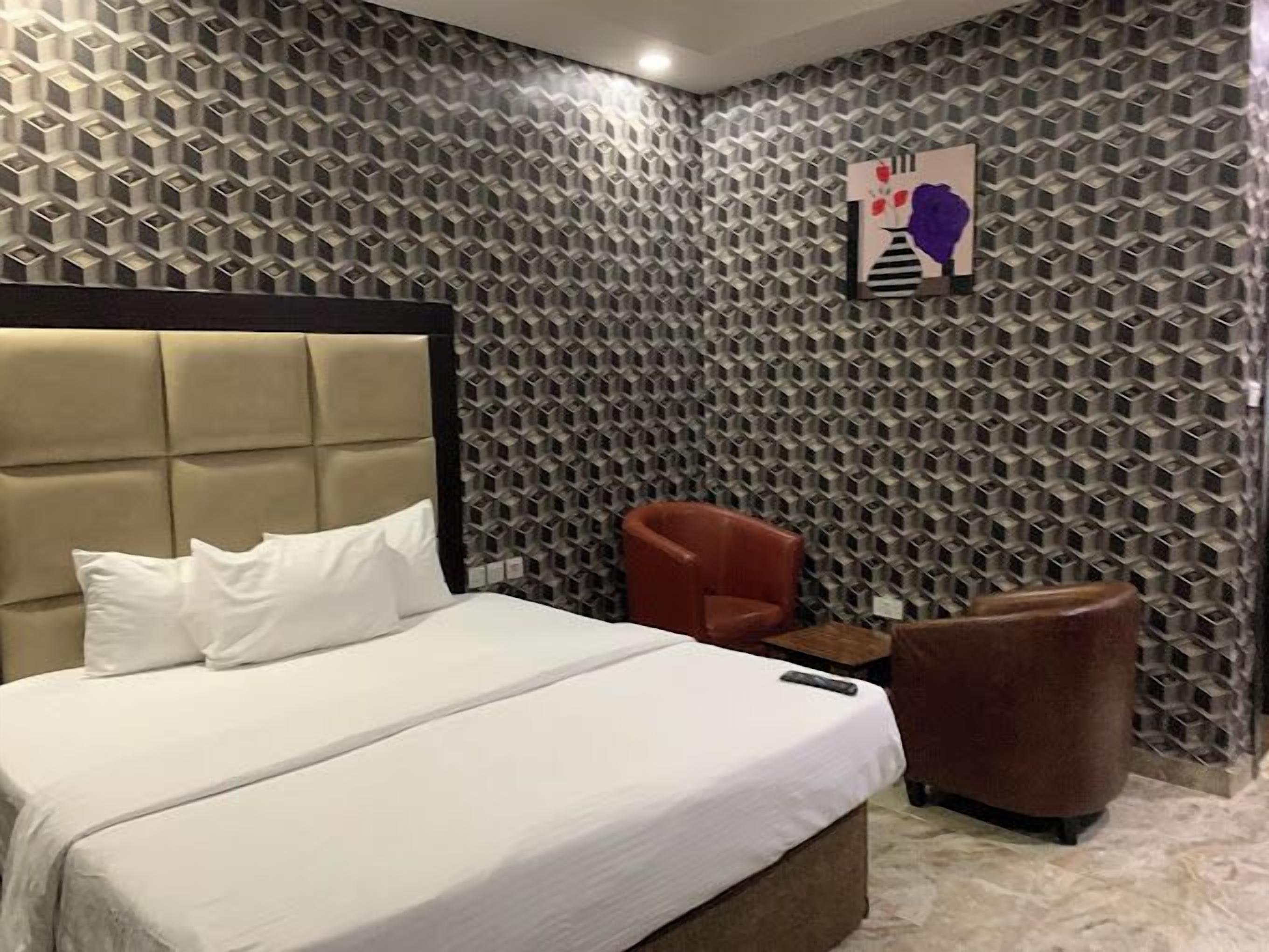Een hotelkamer met een groot bed, een hoofdeinde, een rode fauteuil en een klein tafeltje.