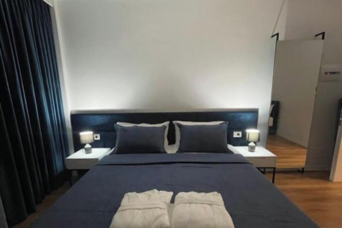 A hotel room with a large bed, two bedside tables, and a dark curtain.