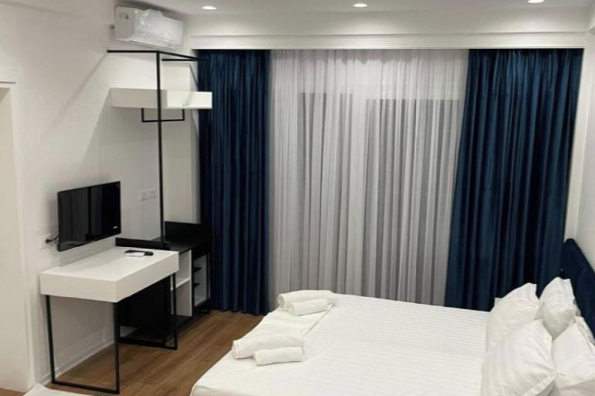 A modern hotel room with a bed, a desk, a TV, and a window with curtains.