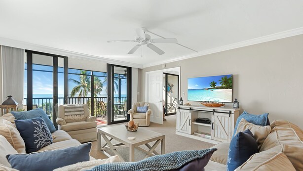 A spacious living room with a large TV, comfortable seating, and a view of the ocean. - Sanibel Beachfront Luxury Condo Full Gulf View! 3BR, 2 BA! Covered Prkg! Sports! (Sanibel)