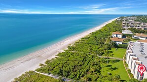 An aerial view of a coastal area with a beach, lush greenery, and a row of buildings with a swimming pool. - Sanibel Beachfront Luxury Condo Full Gulf View! 3BR, 2 BA! Covered Prkg! Sports! (Sanibel)