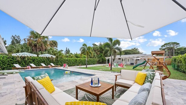 A poolside area with a covered seating area, a pool, and a slide. - PalmParadise: 5BR Family&Pet Fun, HeatedPool&Games (West Palm Beach)
