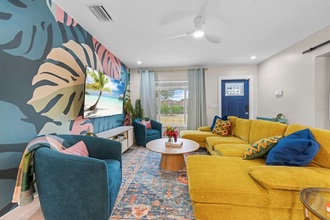 A living room with a tropical mural, a blue sofa, a yellow sofa, and a coffee table.