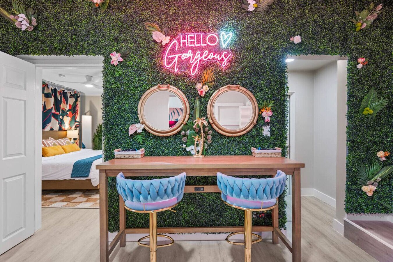 A room with a green wall, two round mirrors, a neon sign, and a bed with a colorful headboard.