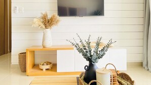 Ein Wohnzimmer mit an der Wand montiertem Fernseher, einem Holz-Konsolentisch und zwei Vasen mit Trockenpflanzen.