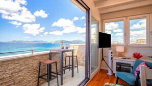 Ein Balkon mit Meerblick, einem Fernseher und einem Tisch mit Stühlen.