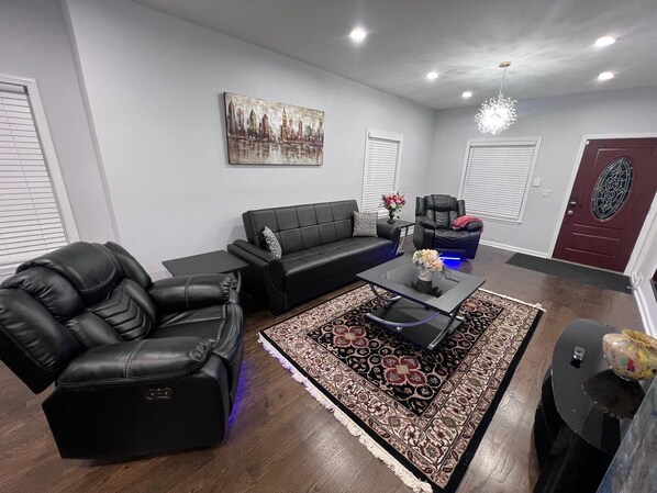 A modern living room with a black leather sofa, a black leather chair, a glass coffee table, and a patterned rug. - Wonderful Entire Home Near Lake In Zion (Zion)