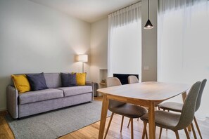 Uma sala de estar moderna com um sofá cinzento, almofadas amarelas, uma mesa de jantar de madeira e cadeiras cinzentas.