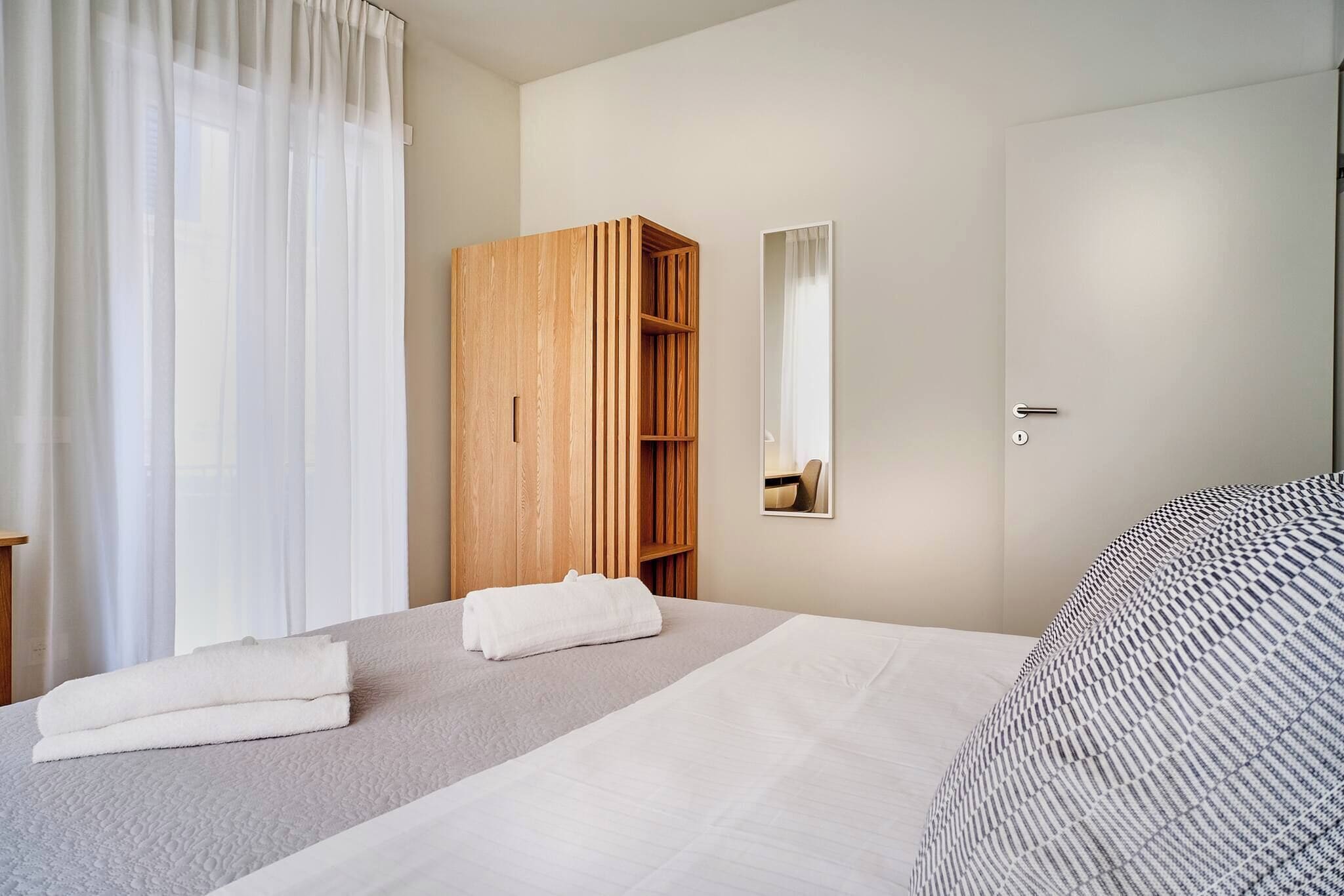 A hotel room with a bed, a wooden wardrobe, a mirror, and a door.