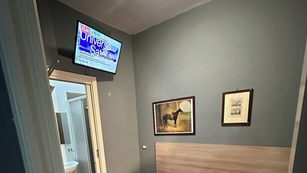 A bedroom with a bed, a red chair, a television mounted on the wall, and a framed picture. - SINGLE APARTMENT 700 METERS FROM THE CENTER OF MILAN (Milano)