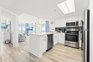 A modern kitchen with white cabinetry, stainless steel appliances, and a large island with a dishwasher.